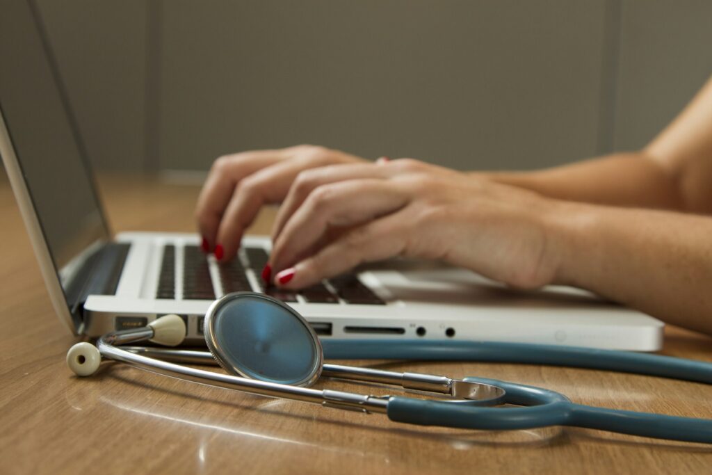 Healthcare professional using a laptop beside a stethoscope